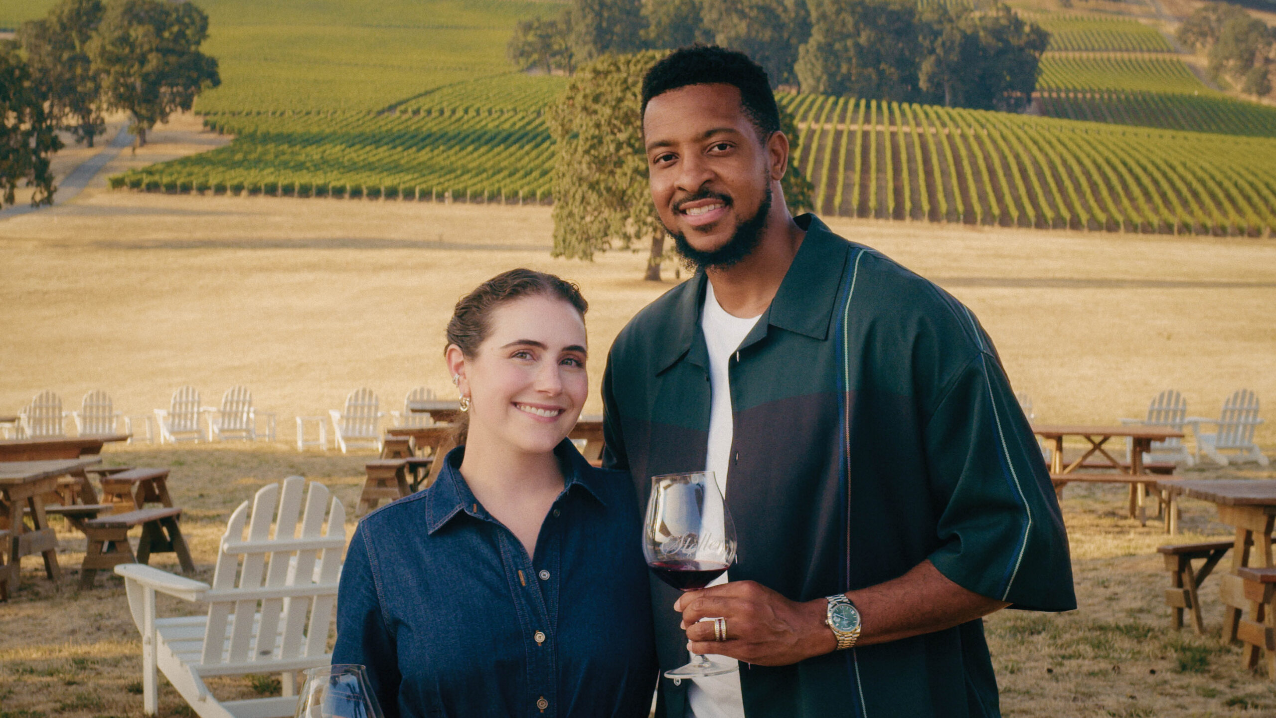 Couple smiling with red wine glasses in front of Stoller Family Estate vineyard rows in Oregon's Dundee Hills