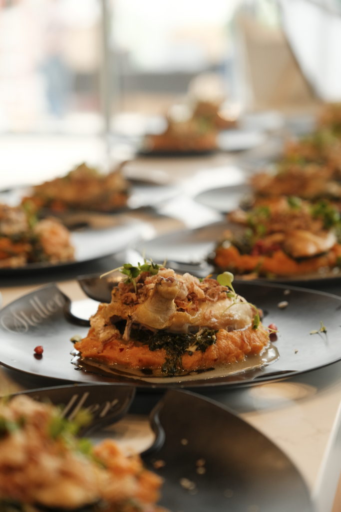 Plated whipped sweet potatoes topped with sautéed greens, roasted chicken, crispy shallots and microgreens on a dark Stoller plate