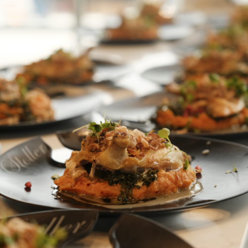 Plated whipped sweet potatoes topped with sautéed greens, roasted chicken, crispy shallots and microgreens on a dark Stoller plate